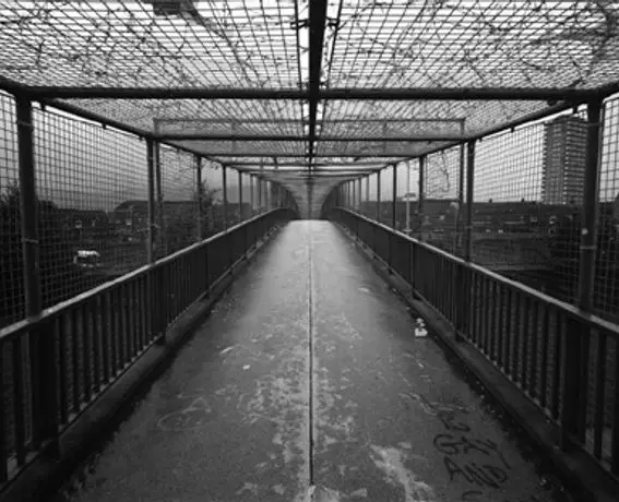 Black and white photograph of a fenced pedestrian bridge by Willie Doherty, exploring memory, control, and mental health in Derry.